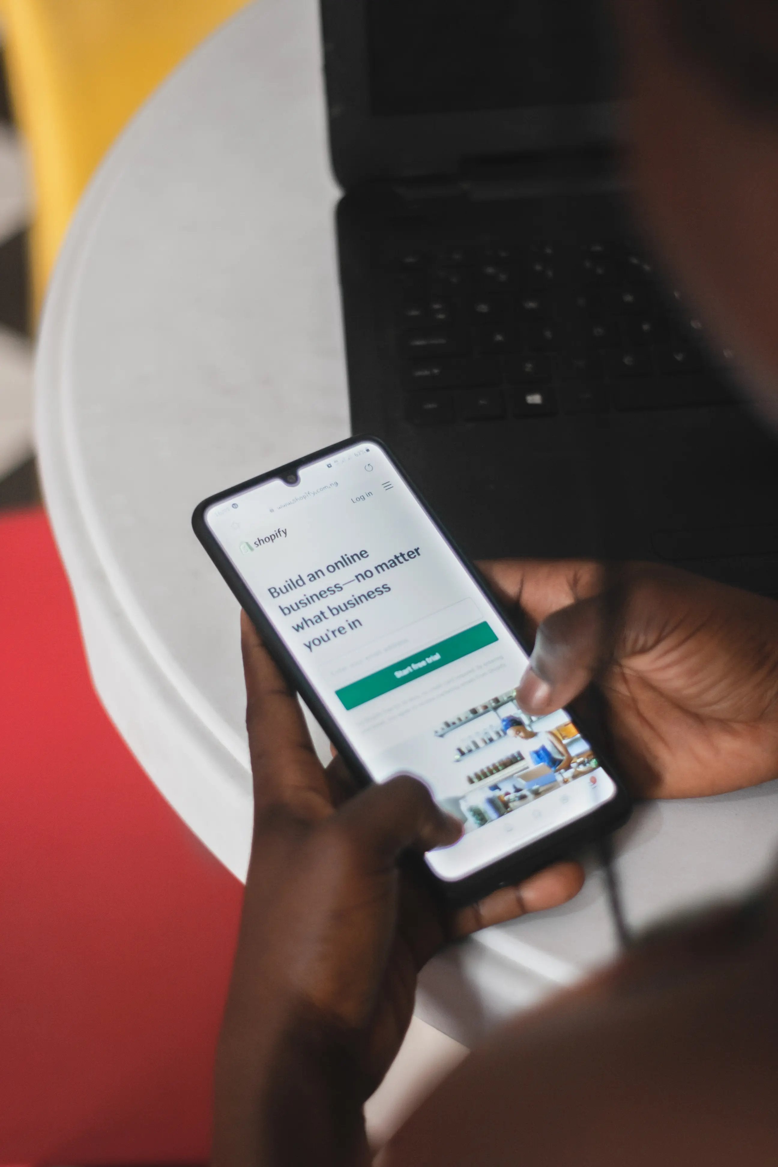 A man is holding a cell phone showing shopify home page